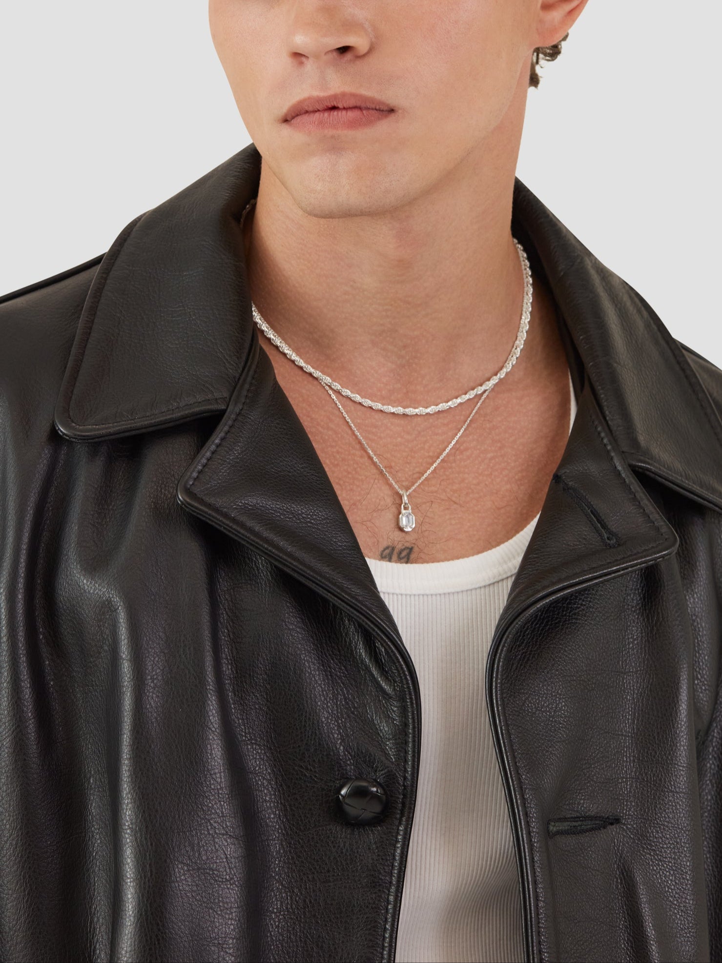 Man wearing a black leather jacket and silver necklaces on a plain background