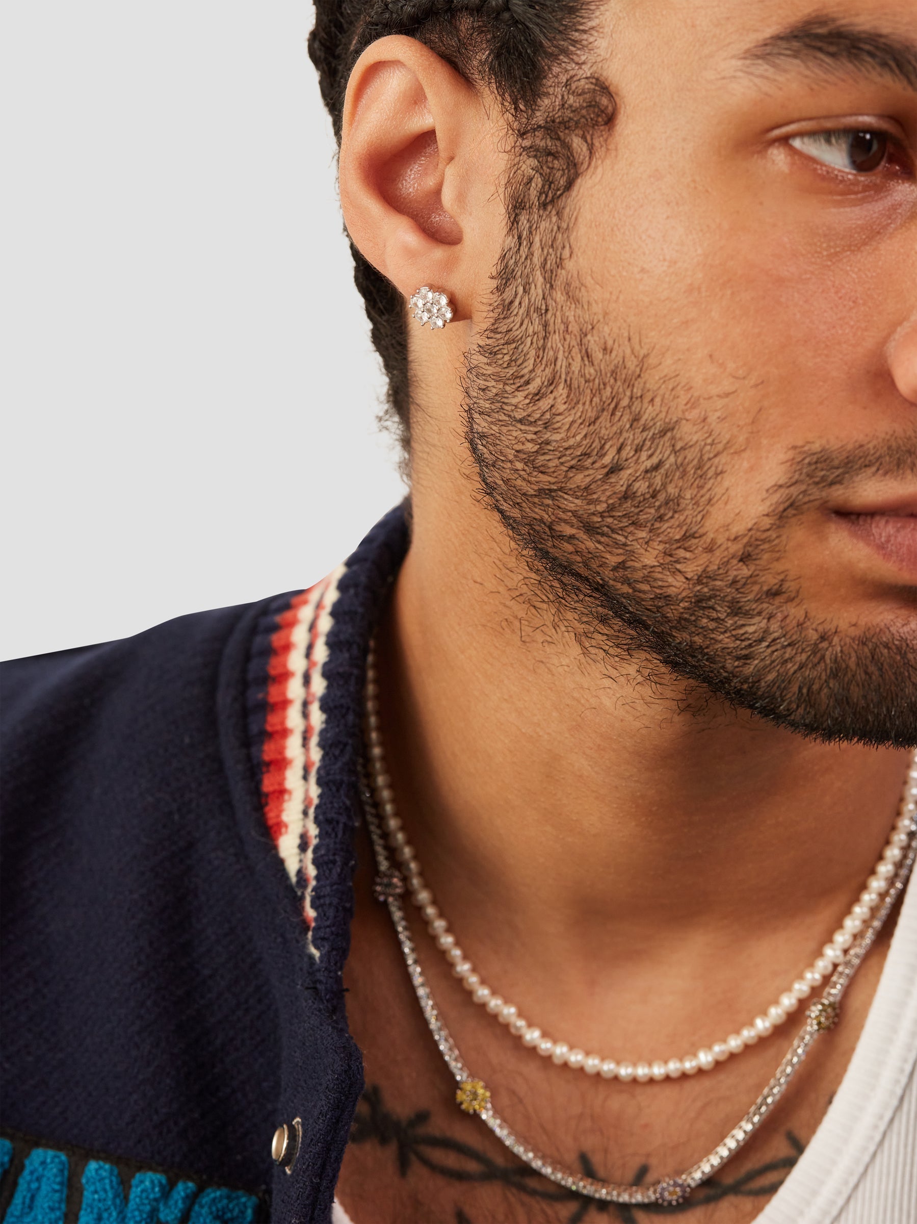 Close-up of a man wearing pearl necklaces and an earring against a neutral background